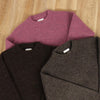 Three folded sweaters in purple, brown, and gray on a wooden surface