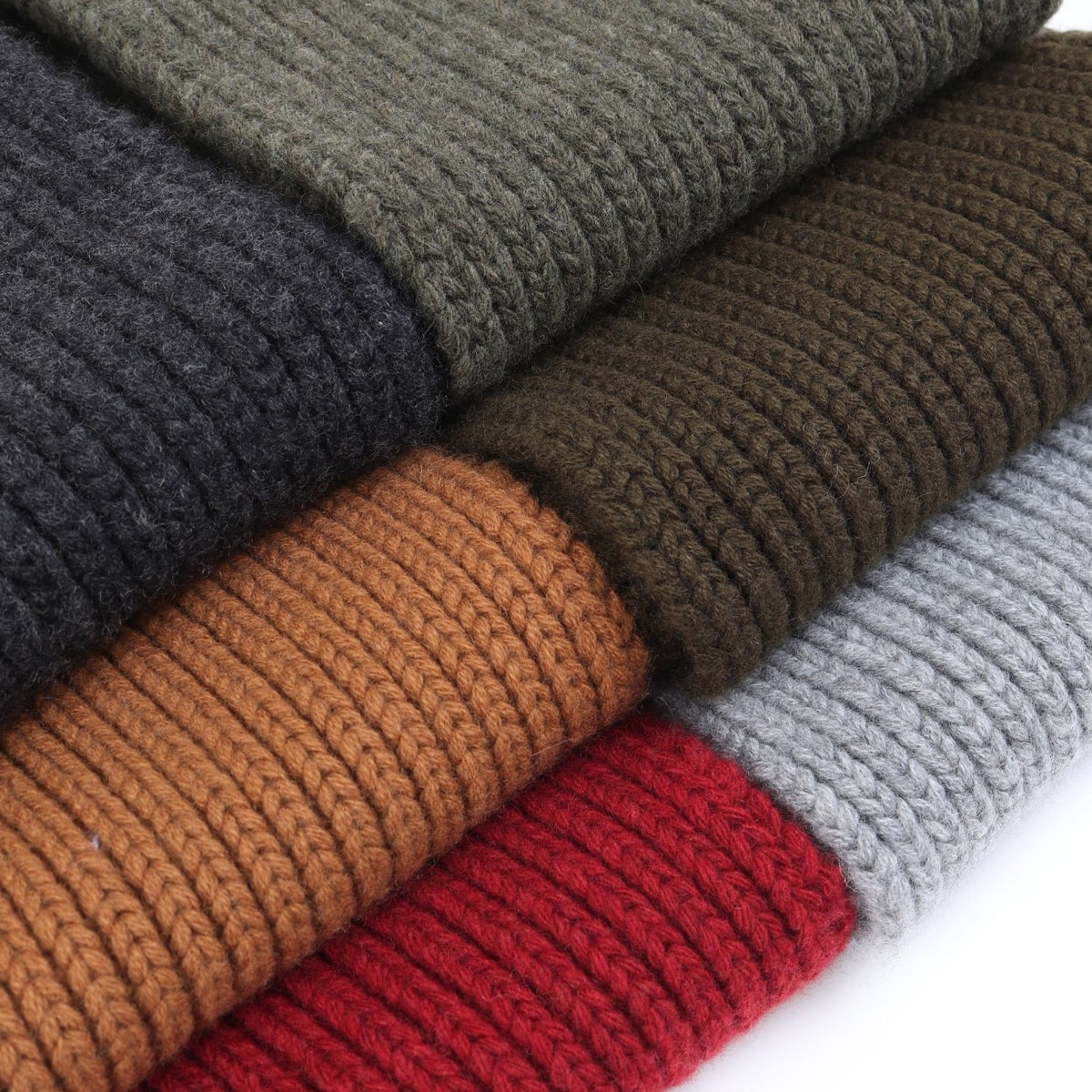 Stack of folded knit scarves in various colours on a white background