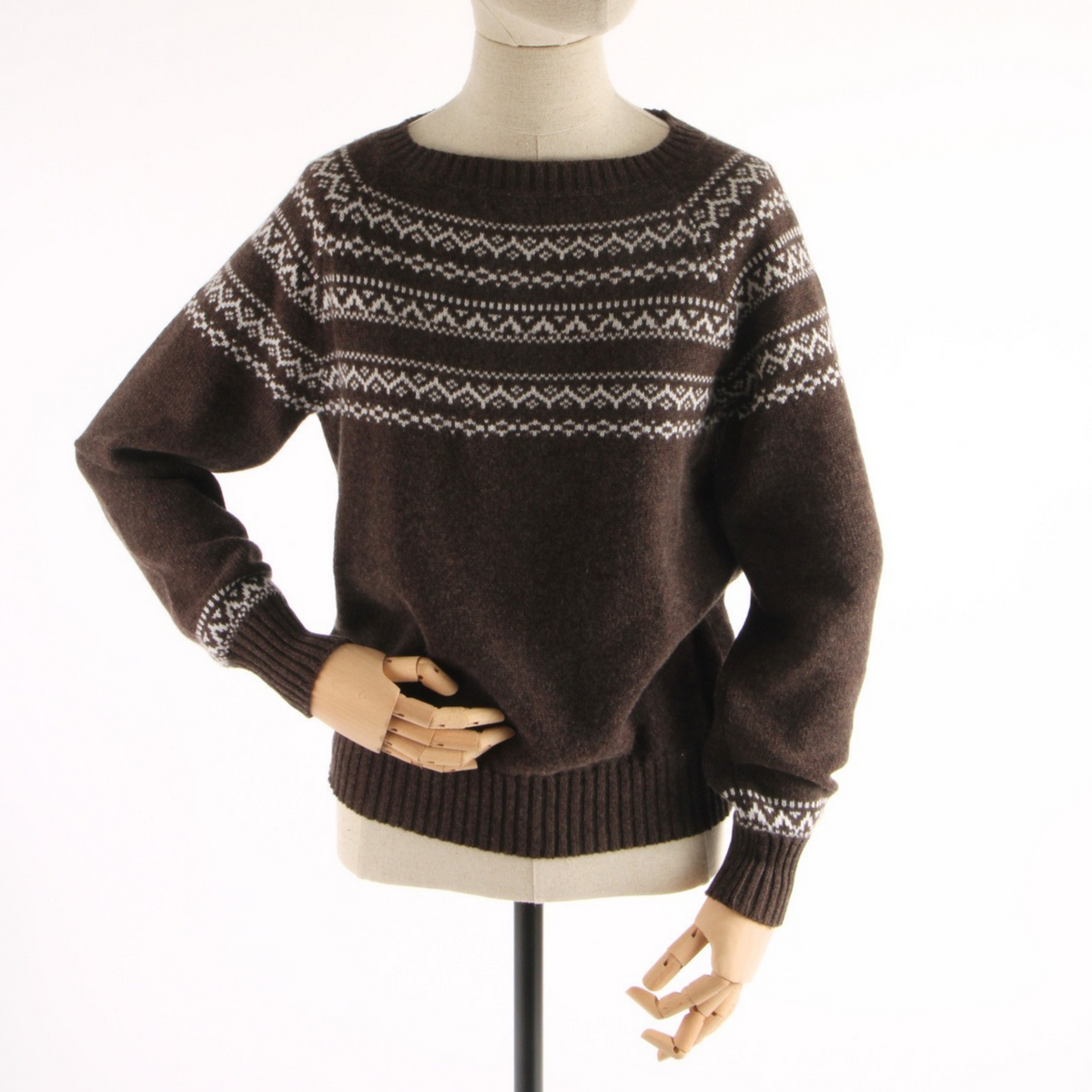 A dark brown knit sweater with a cream Fair Isle pattern across the chest and cuffs, displayed on a mannequin torso against a white background.