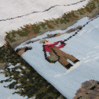 knitted design of a person in a red top and hat standing in the river fishing