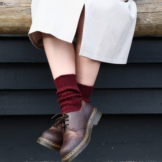 Person wearing maroon wool socks and brown leather shoes sitting on a wooden bench.