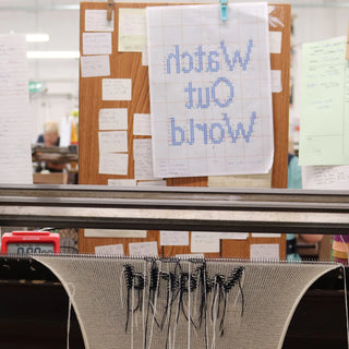 knitted fabric with 'watch out world' knitting on a loom in a workshop setting