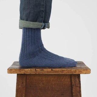 person wearing denim blue wool & cotton socks on a wooden stool