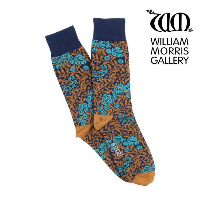 A pair of patterned socks featuring the William Morris Michaelmas Daisy design with blue and gold patterns on a brown background, displayed with the William Morris Gallery branding.