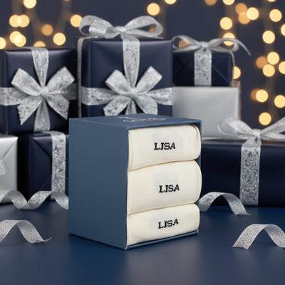 Three folded personalized socks with the name 'LISA' knitted on the side, displayed on a wooden surface.
