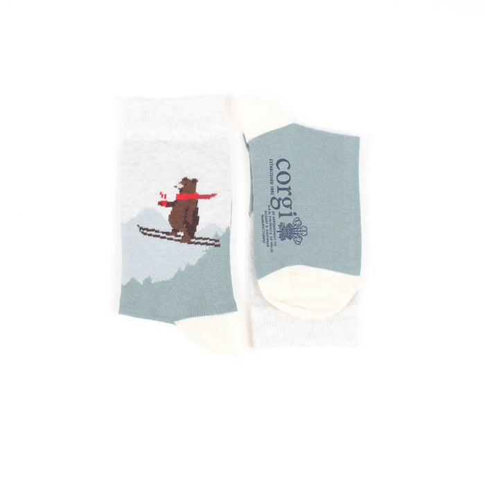 A pair of kids' socks with a skiing bear design, placed against a Christmas-themed backdrop with holiday ornaments.