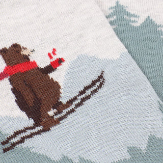 Knitted fabric with a bear design wearing a red scarf and skis on a snowy background.