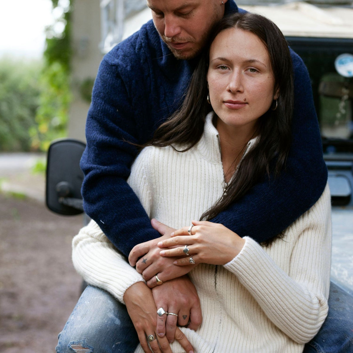A woman wearing a white ribbed zip cashmere cardigan with a stand-up collar, long sleeves, and ribbed cuffs. She is sitting and holding hands with a man who is partially visible.