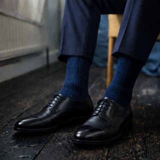 Person wearing black dress shoes and blue socks on a wooden floor.