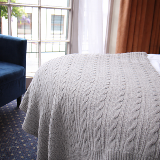Gray cable knit blanket draped over a chair in a room with a blue couch and window.