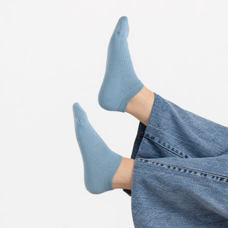 Light blue socks worn with denim jeans on a light gray background