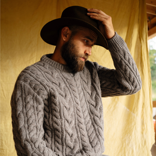 Man wearing a brown cable knit sweater and dark hat indoors.