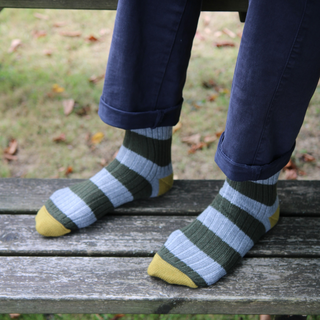 Striped socks with green, grey, and yellow pattern worn on a wooden bench.
