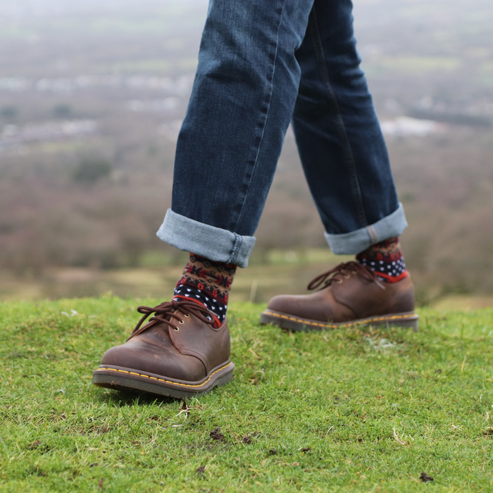 Person wearing brown boots and patterned socks standing on grass with a blurred landscape in the background