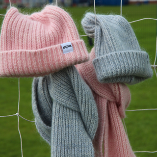 Pink and grey knit hats with scarves hanging on a football net against a grassy background