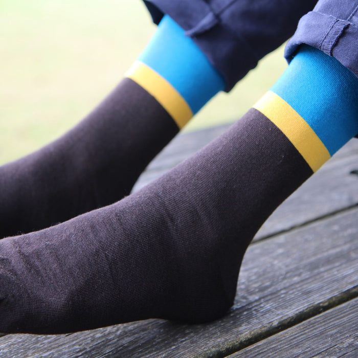 Close-up of chocolate brown socks with blue and yellow stripes on a wooden surface.