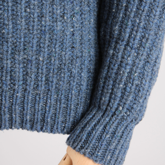 Close-up of a blue knitted sweater sleeve on a light gray background