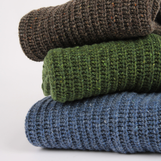Stack of three folded knitted sweaters in brown, green, and blue on a white background