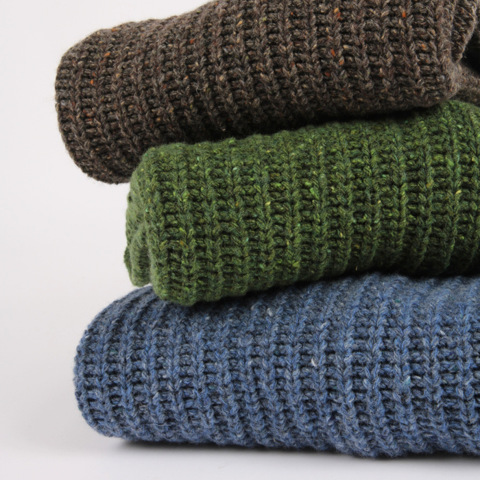 Stack of three folded knitted sweaters in brown, green, and blue on a white background