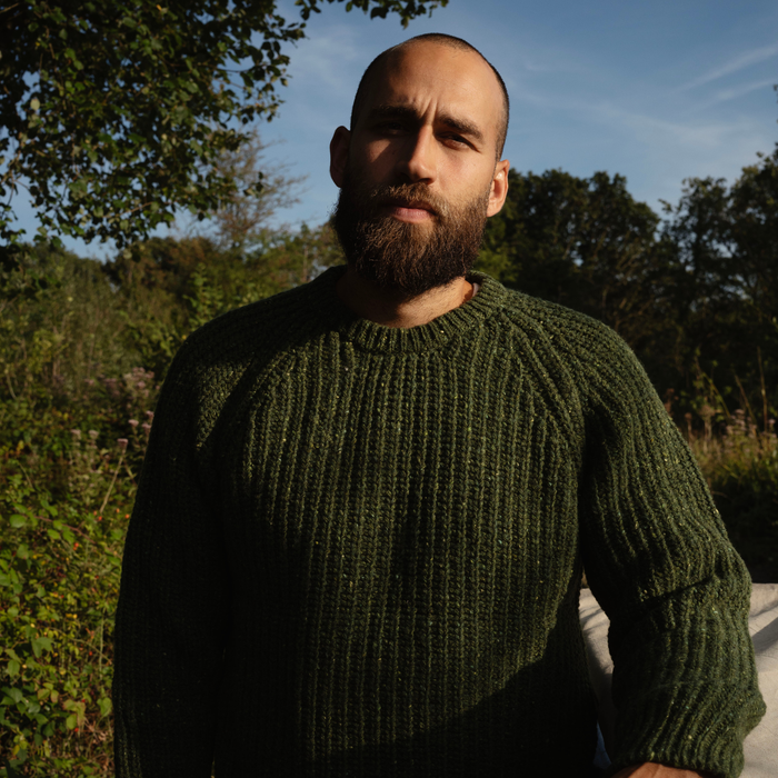 Man wearing a green sweater standing outdoors with trees in the background