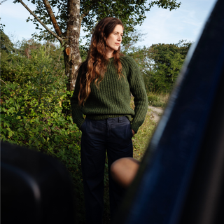 Woman in a green sweater standing outdoors with trees in the background
