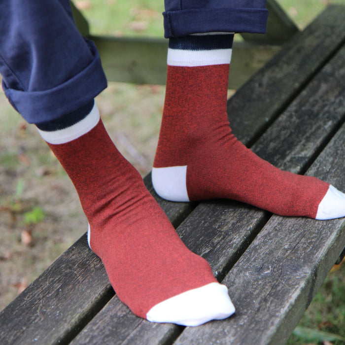 Red socks with white accents worn by a person sitting on a wooden bench.