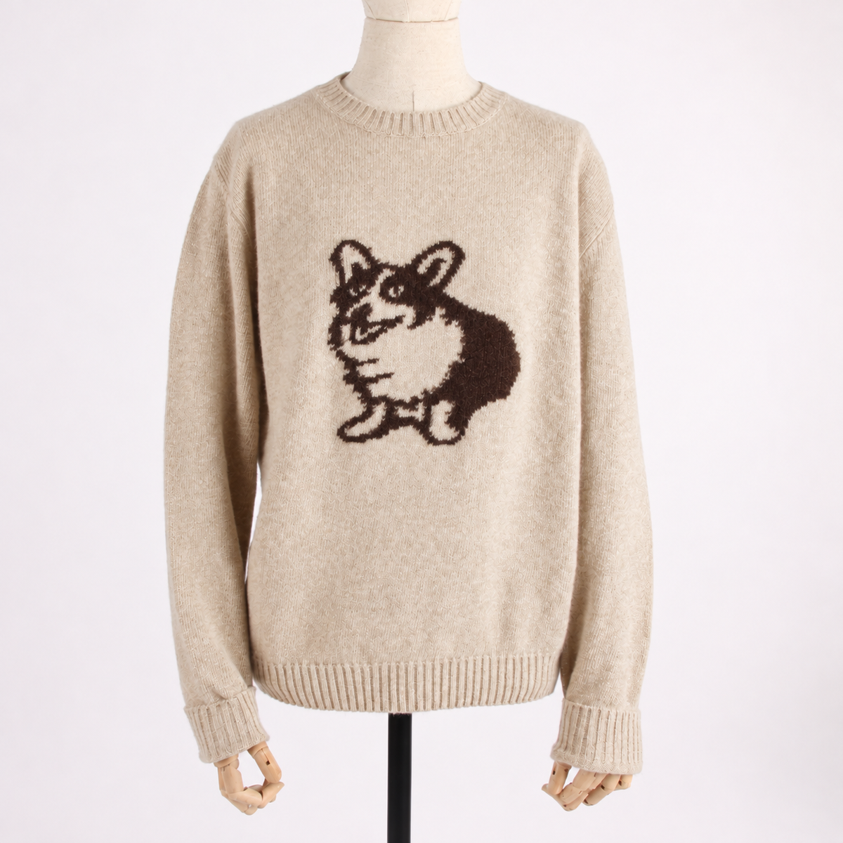 A cream-colored knit sweater displayed on a mannequin, featuring a dark brown knitted corgi graphic on the chest.