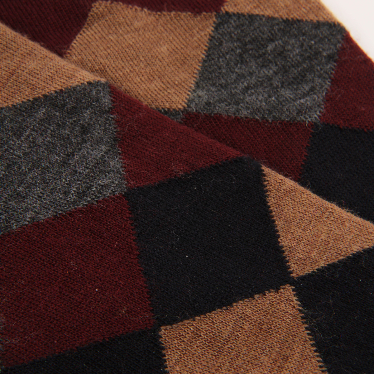 A close-up of a textured knit fabric with a large check pattern in dark red, black, tan, and charcoal gray.