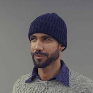 Man wearing a blue knit beanie and gray sweater against a gray background
