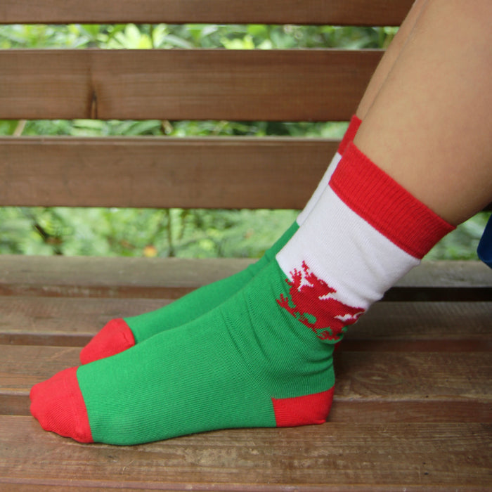 Green and red socks with a white cuff featuring a dragon Welsh flag design on a wooden bench.