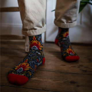 A person wearing patterned cotton socks with red tips and a floral design, standing on a wooden floor.