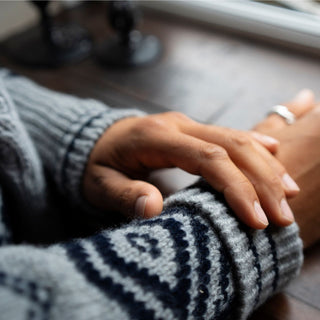 Close-up of two hands, one wearing a patterned sweater, on a wooden surface.