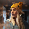 A woman wearing a yellow ribbed wool beanie with a pom pom on top.