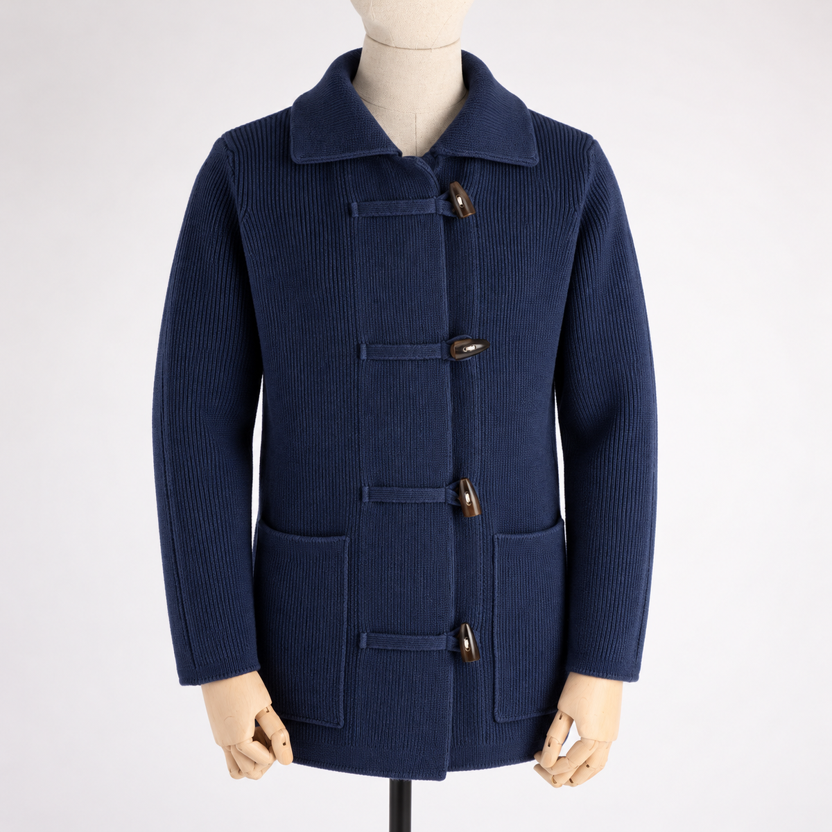 A navy blue ribbed knit duffle coat with brown wooden toggle buttons, displayed on a mannequin against a light gray background.