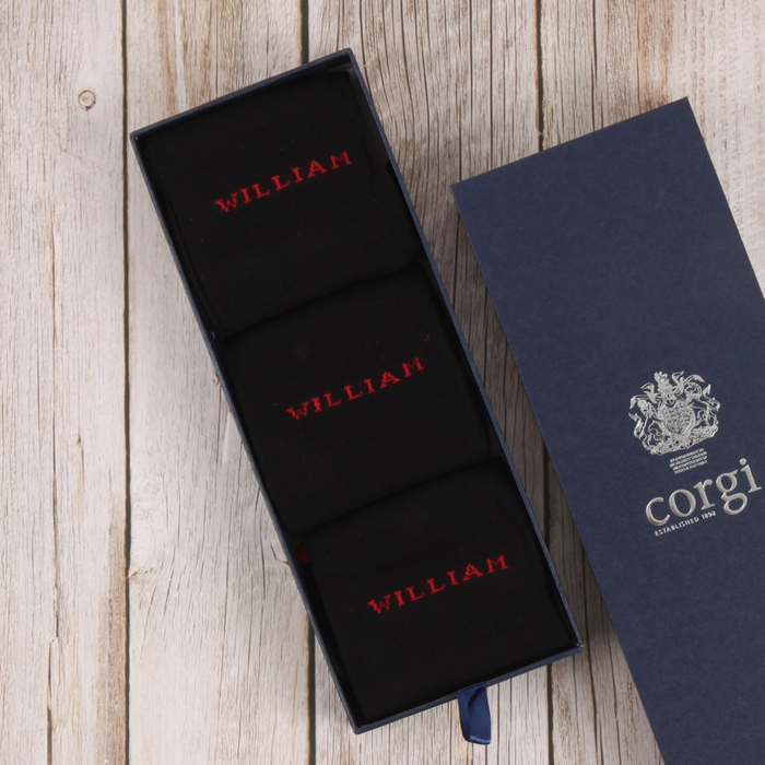 Navy socks with 'WILLIAM' embroidery in red text, inside an open navy box with 'Corgi' branding.