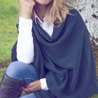A woman wearing a dark green cashmere poncho over a white shirt and blue jeans, with brown boots.