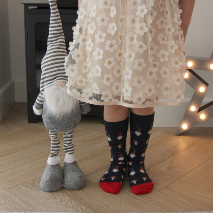 Person wearing a floral dress and patterned socks next to a gnome on a wooden floor.