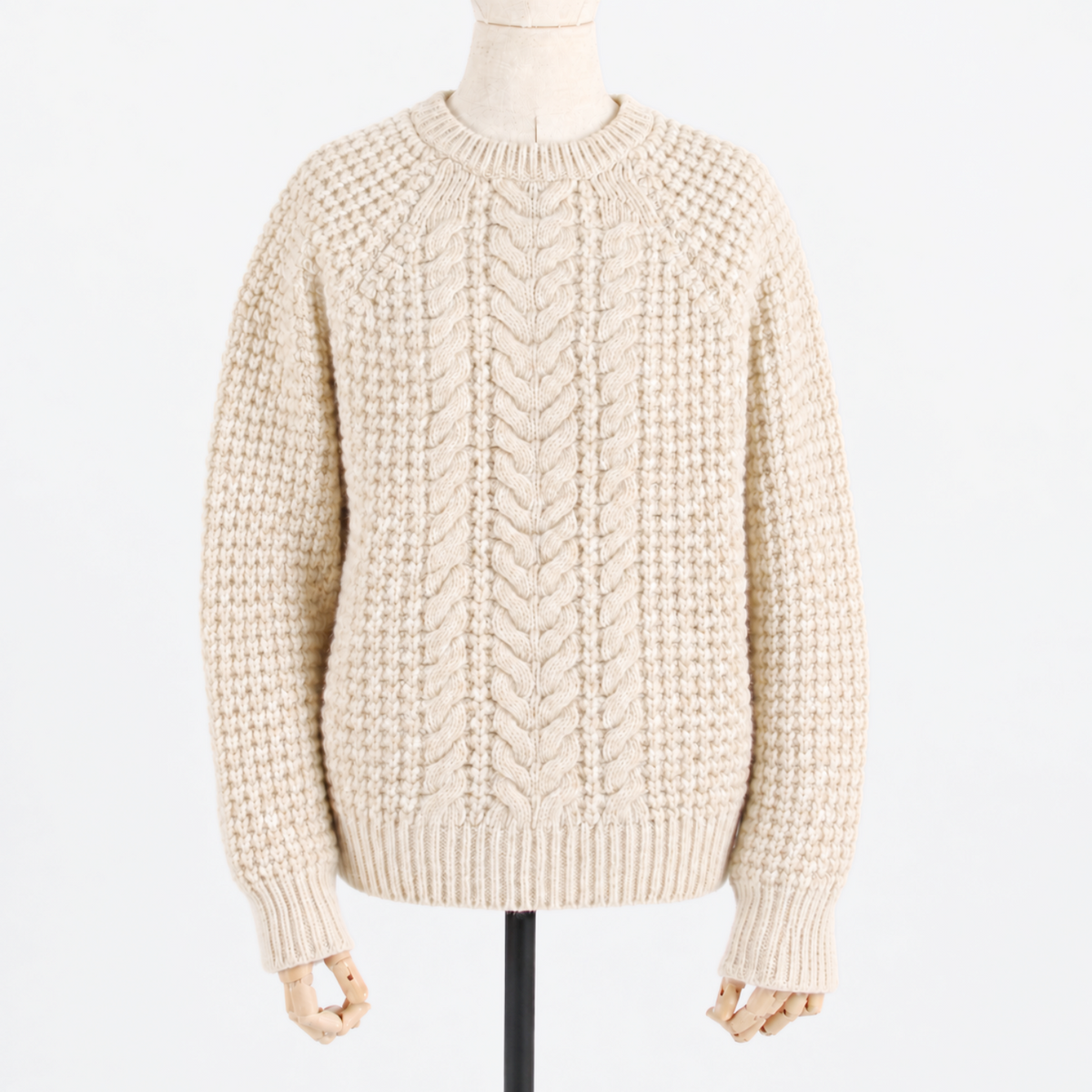 A cream-colored chunky cable-knit sweater displayed on a mannequin against a plain white background.