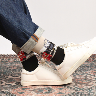 Person wearing white sneakers with a London scene socks on a patterned rug
