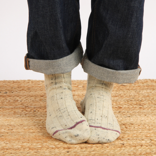 Person wearing beige socks with dark jeans on a woven surface
