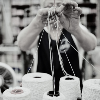 a person standing at a knitting machine with spools of yarn