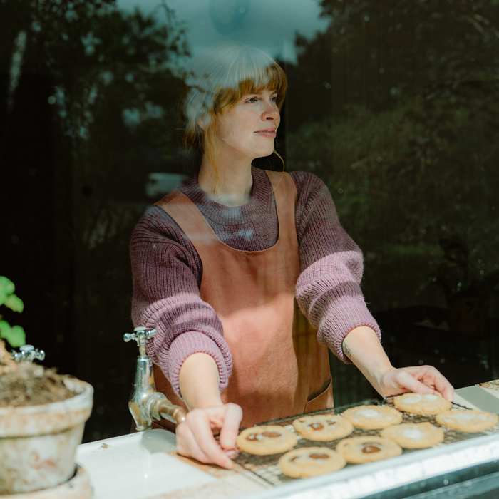 Woman in a pink sweater and apron arranging cookies on a tray outdoors.
