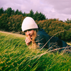 Person wearing a white beanie and dark jacket in a grassy field with trees in the background