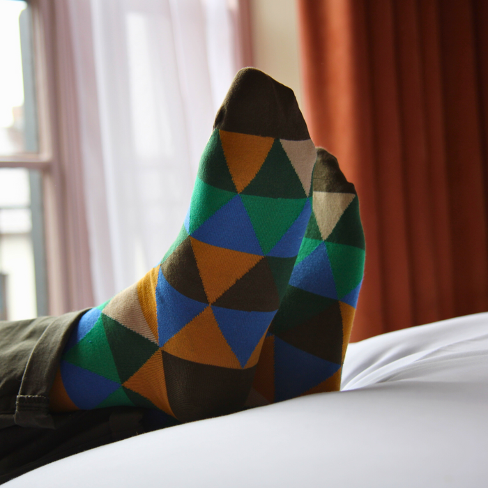Colorful geometric-patterned socks on a person sitting by a window with curtains.