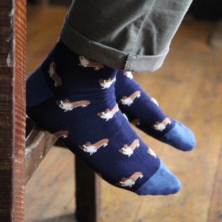 Navy blue socks with corgi dog pattern worn by a person on a wooden floor.