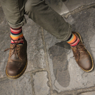 Person wearing brown leather boots and colorful striped socks on a stone pavement.