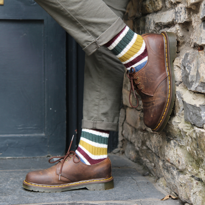 Person wearing brown shoes and colorful striped socks against a stone wall.