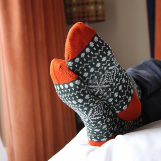 Person wearing patterned socks with orange toes and heels, sitting on a bed.