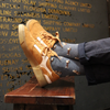 Brown suede sneaker with white laces on a wooden stool against a textured wall with text.