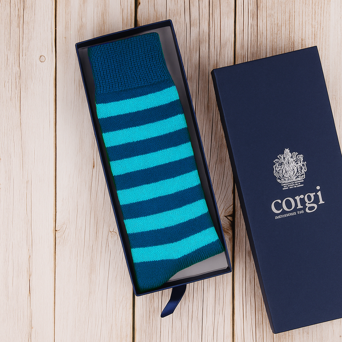 Blue and green striped sock in an open box with 'corgi' branding on a wooden surface